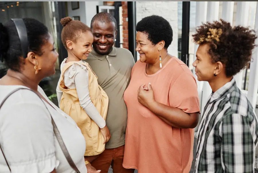 Group of 5 people smiling and standing around a man holding a young child.
